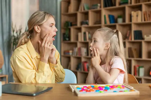 Professional woman speech therapist studying together with pretty little girl learning practice pronunciation exercises