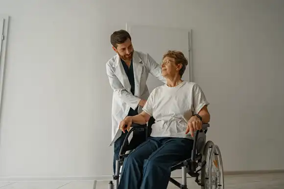 Professional male doctor carrying female patient on wheelchair in medicine clinic hall
