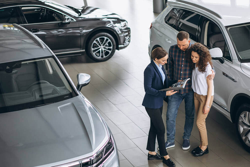 Young Couple Talking SalesPerson at Car Showroom